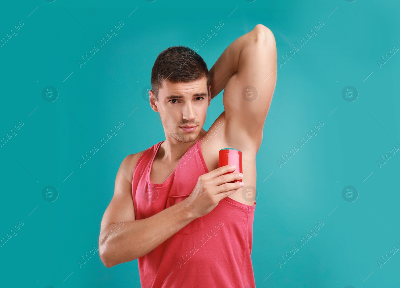 Photo of Young man applying deodorant to armpit on light blue background