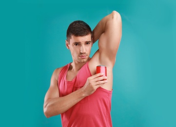 Photo of Young man applying deodorant to armpit on light blue background