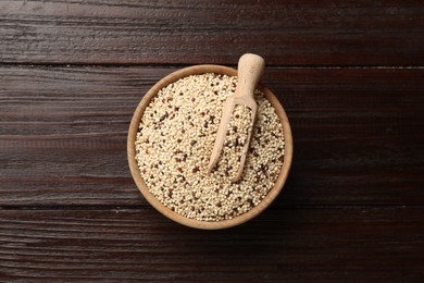 Photo of Raw quinoa seeds and scoop in bowl on wooden table, top view