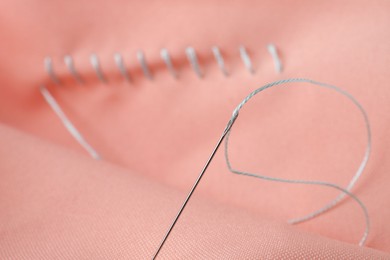 Photo of Sewing needle with thread and stitches on coral cloth, selective focus
