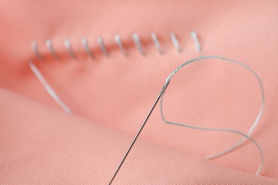 Sewing needle with thread and stitches on coral cloth, selective focus