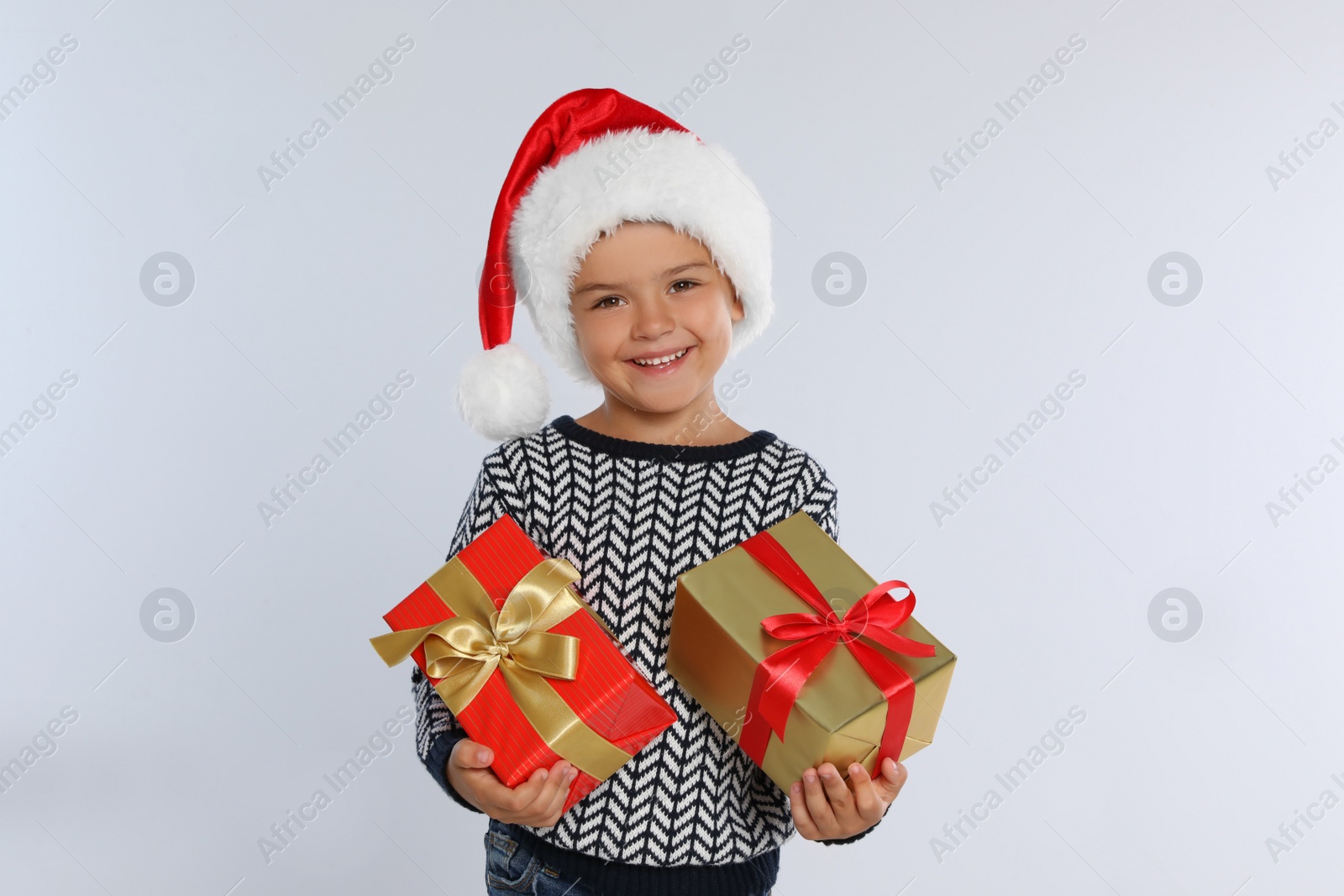 Photo of Happy little child in Santa hat with gift boxes on light grey background. Christmas celebration