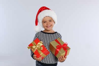 Photo of Happy little child in Santa hat with gift boxes on light grey background. Christmas celebration