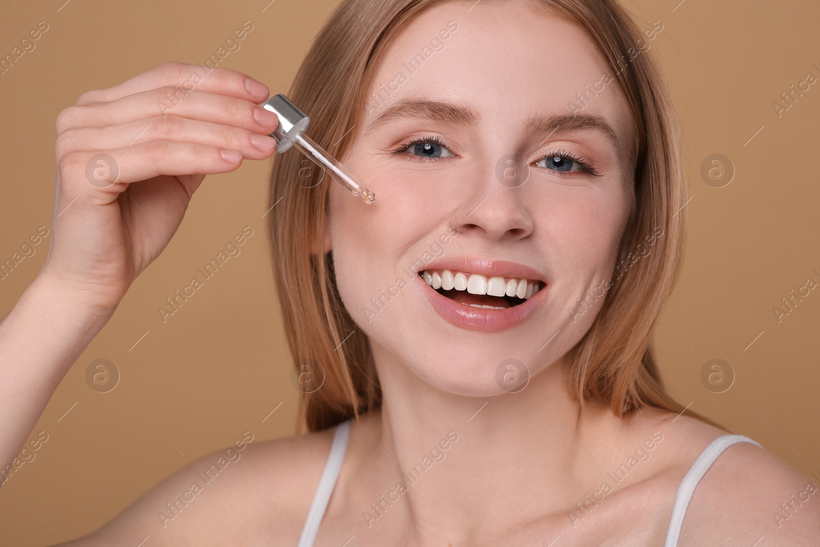 Photo of Woman applying essential oil onto face on light brown background