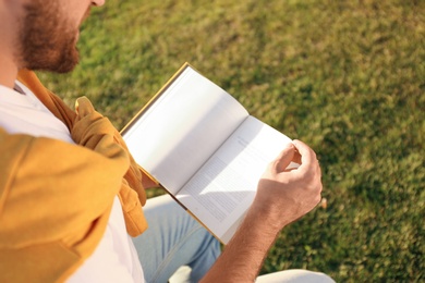 Young man reading book outdoors on sunny day, closeup