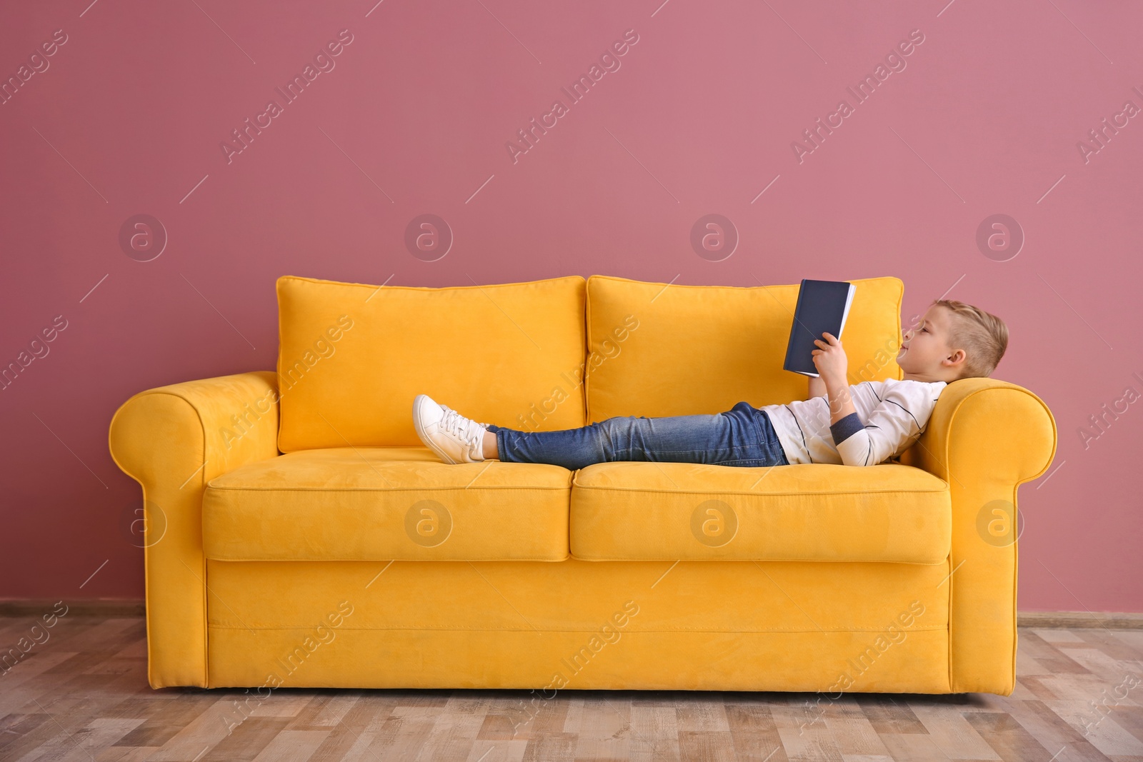 Photo of Cute little boy lying on sofa and reading book, indoors