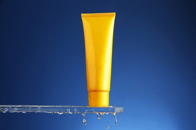 Moisturizing cream in tube on glass with water drops against blue background. Space for text