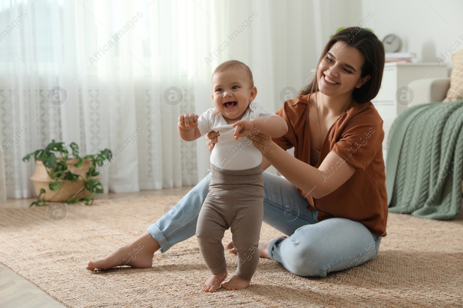 Photo of Mother supporting her baby daughter while she learning to walk at home