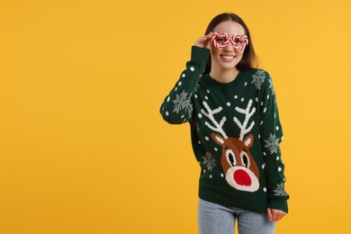 Happy young woman in Christmas sweater and funny glasses on orange background. Space for text