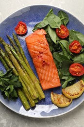 Photo of Tasty grilled salmon with tomatoes, asparagus lemon and basil on grey table, top view