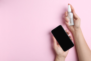 Photo of Woman with smartphone and antiseptic spray on pink background, top view. Space for text