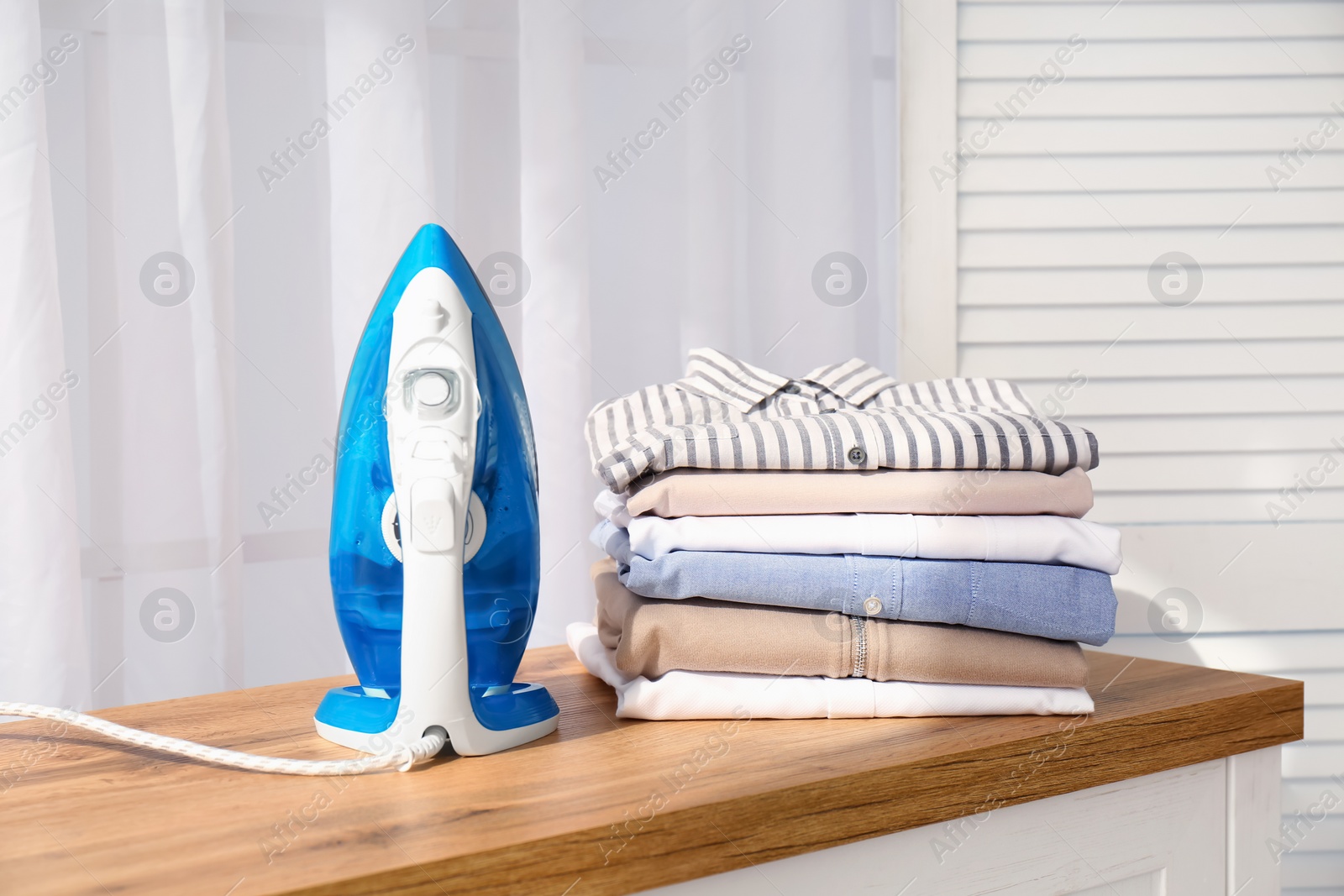 Photo of Stack of clean clothes and iron on board indoors