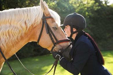 Young woman in horse riding suit and her beautiful pet outdoors on sunny day