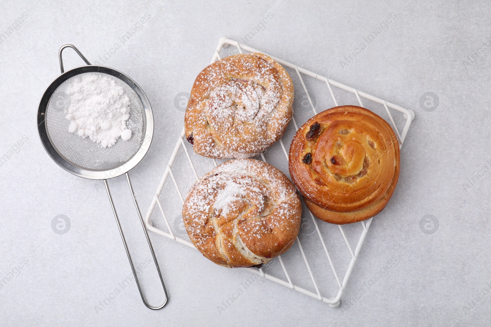 Photo of Different delicious rolls with sugar powder on light grey table, flat lay. Sweet buns