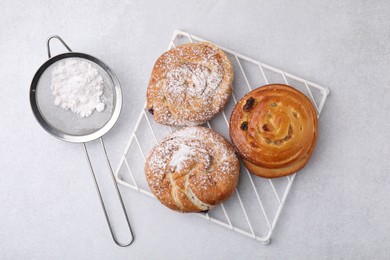 Different delicious rolls with sugar powder on light grey table, flat lay. Sweet buns