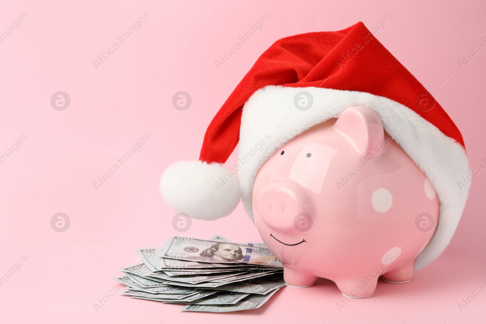 Photo of Piggy bank with Santa hat and dollar banknotes on pink background. Space for text