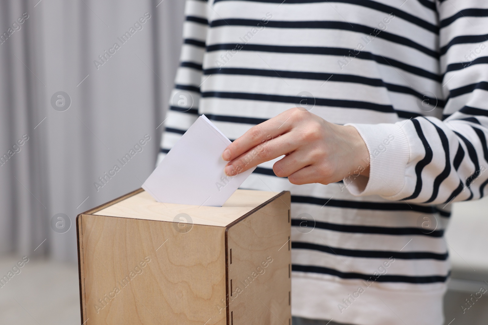 Photo of Woman putting her vote into ballot box on blurred background, closeup