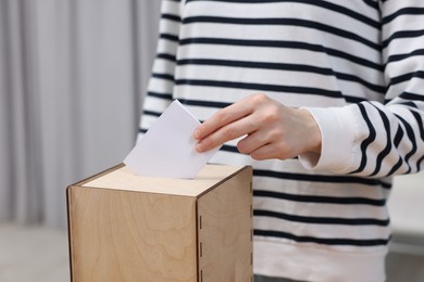 Photo of Woman putting her vote into ballot box on blurred background, closeup