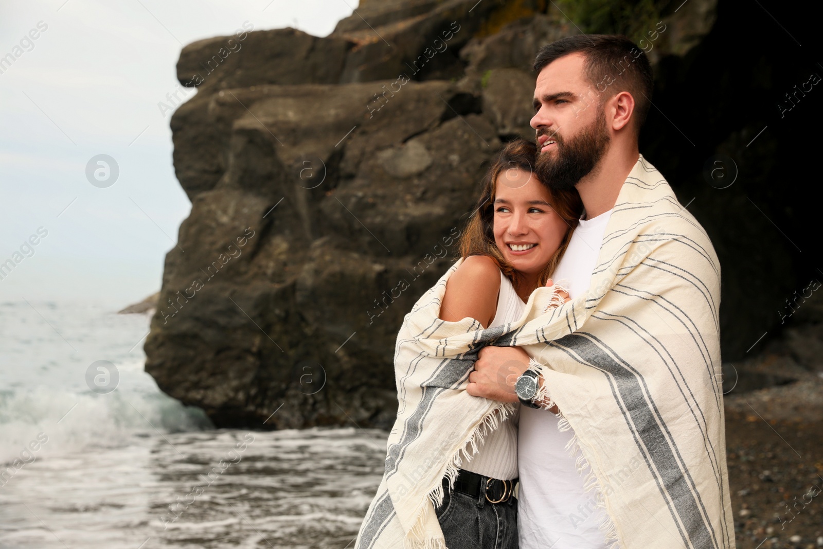 Photo of Happy young couple with blanket on beach near sea. Space for text