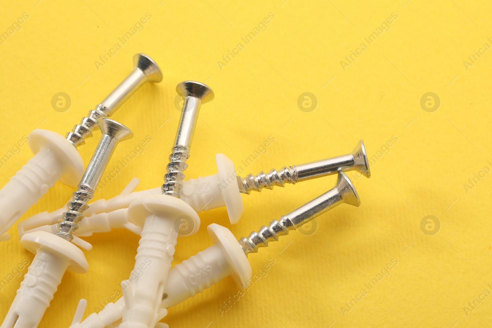 Photo of Many metal screws and white straddling dowels on yellow background, closeup