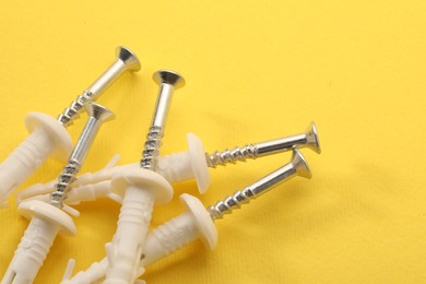 Photo of Many metal screws and white straddling dowels on yellow background, closeup