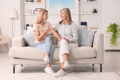 Photo of Happy mature mother and her daughter talking on sofa at home