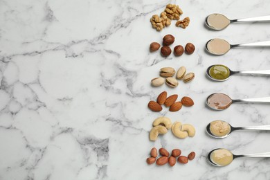 Jars with butters made of different nuts and ingredients on white marble table, flat lay. Space for text