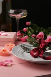 Place setting with roses and candles on pink wooden table, closeup. Romantic dinner