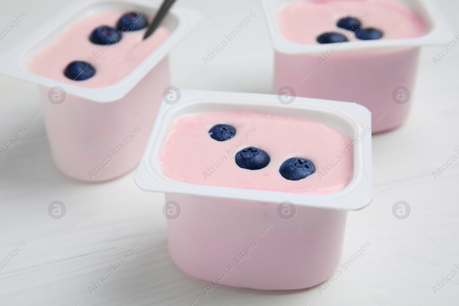 Photo of Plastic cups with tasty yogurts and blueberries on white wooden table