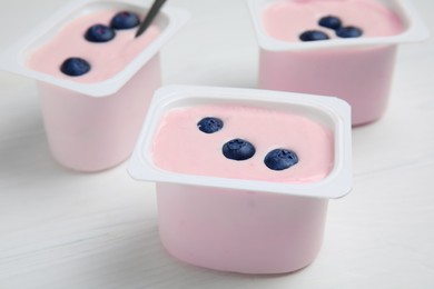 Plastic cups with tasty yogurts and blueberries on white wooden table