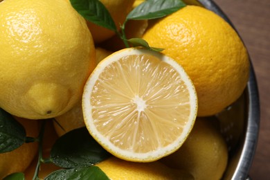 Fresh lemons and green leaves in colander on table, closeup