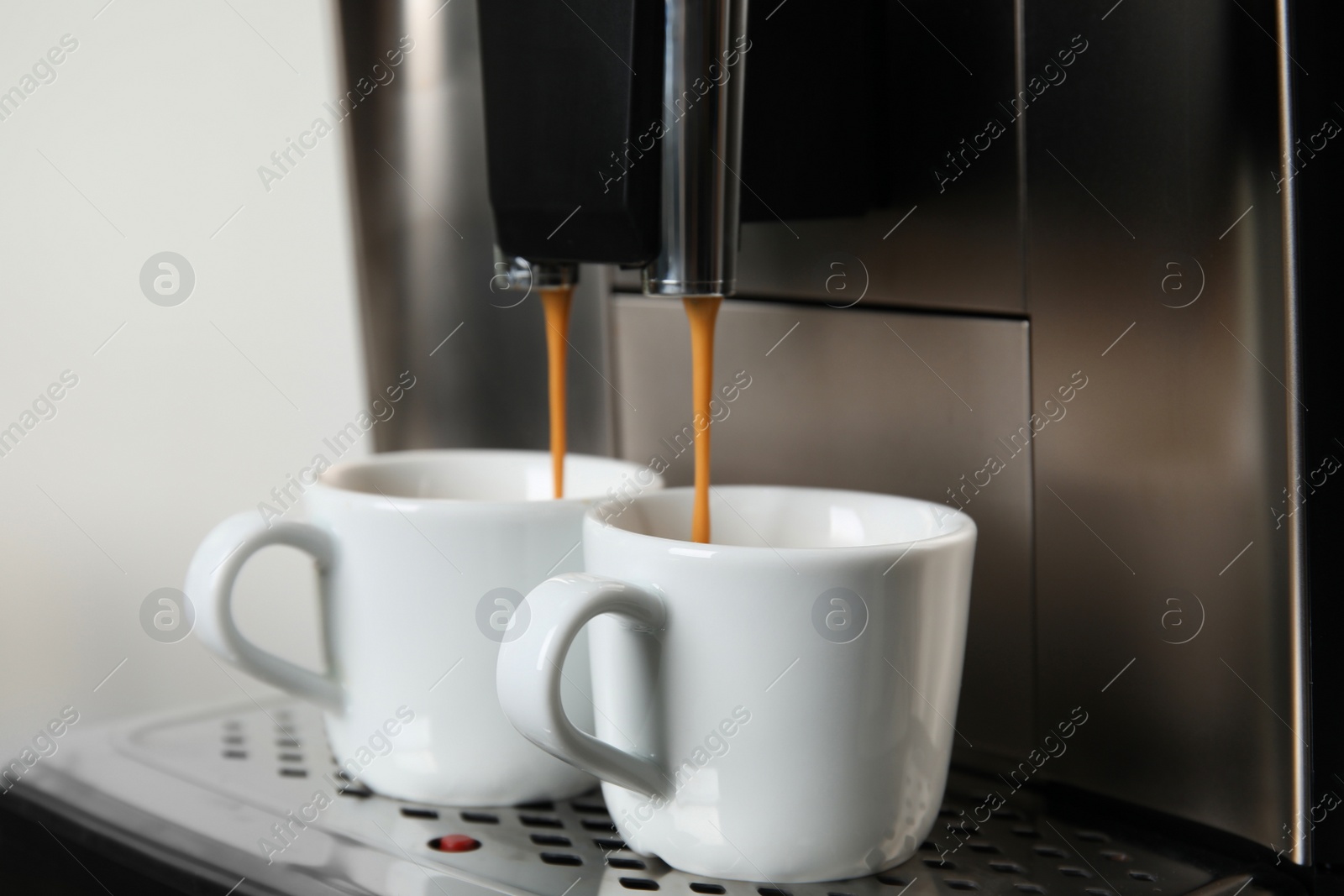 Photo of Espresso machine pouring coffee into cups against light background, closeup