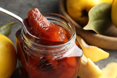 Photo of Taking tasty homemade quince jam from jar at table, closeup