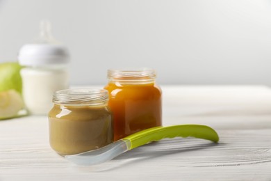 Photo of Jars with healthy baby food and spoon on white wooden table