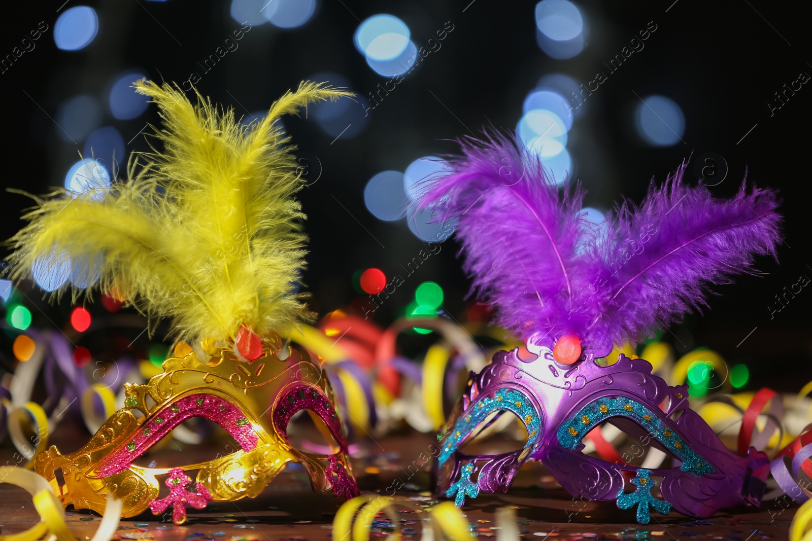 Photo of Beautiful carnival masks and party decor on table against blurred lights