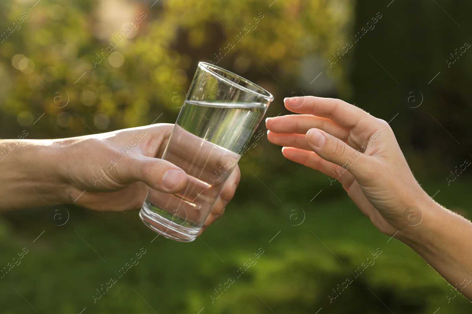 Photo of Man giving glass of fresh water to woman outdoors, closeup