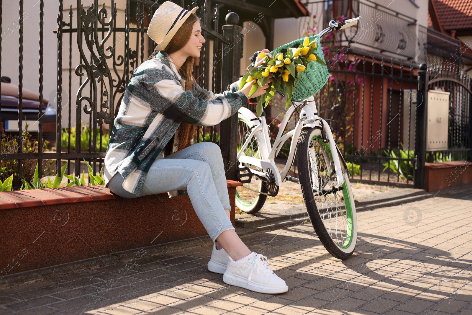 Photo of Beautiful teenage girl with bouquet of yellow tulips and bicycle on city street