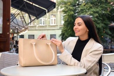 Photo of Young woman with stylish bag at table in outdoor cafe