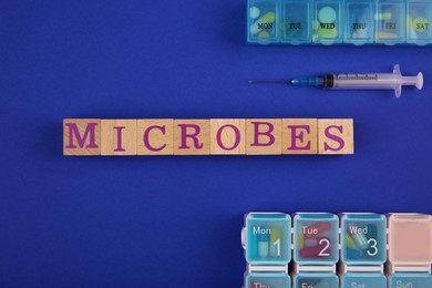 Photo of Word Microbes made with wooden cubes, syringe and pill boxes on blue background, top view