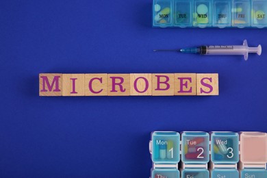 Word Microbes made with wooden cubes, syringe and pill boxes on blue background, top view