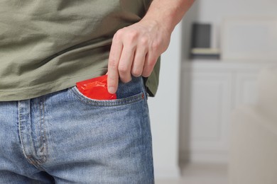 Man pulling condom out of pocket indoors, closeup. Space for text