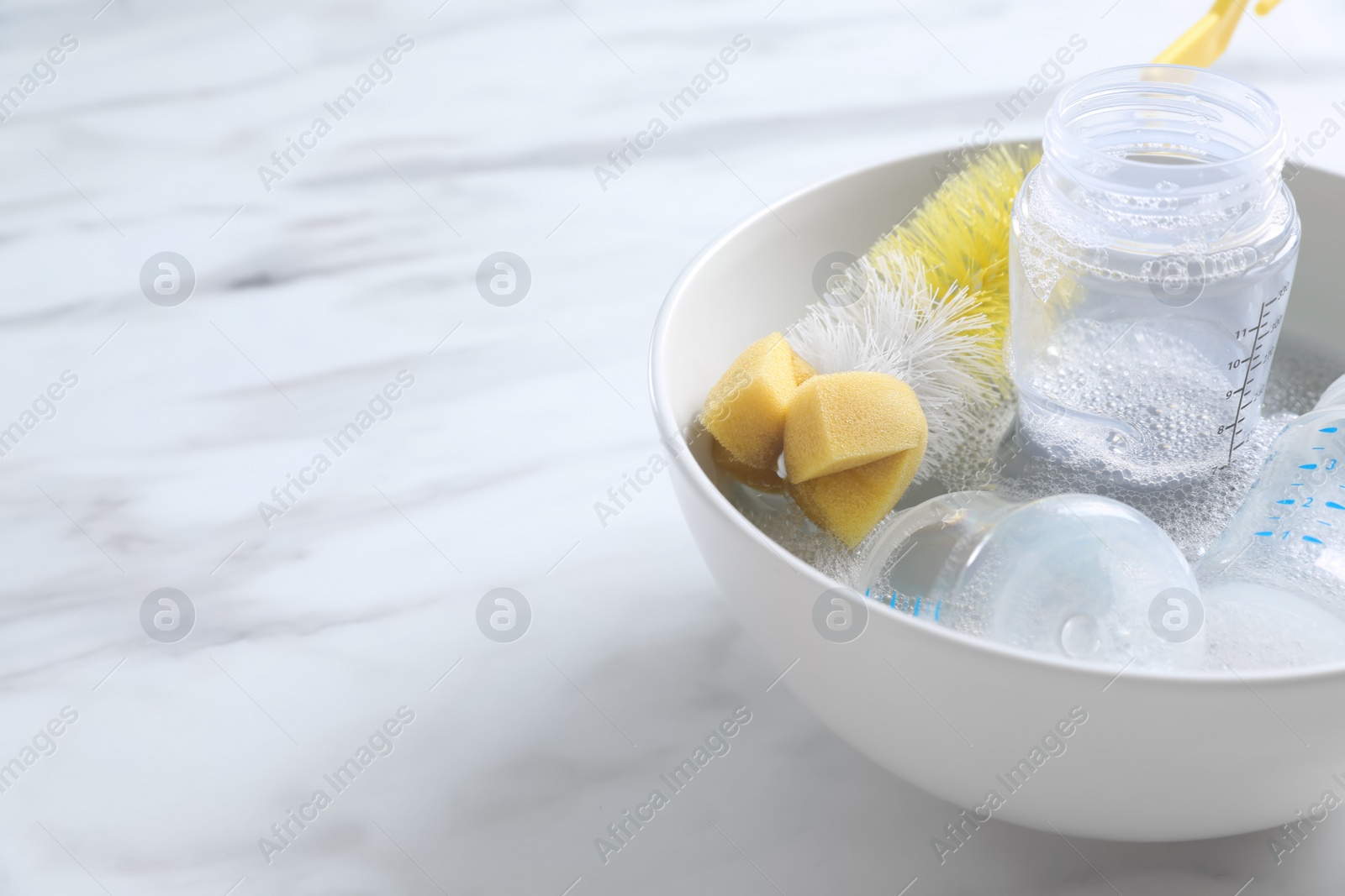 Photo of Bowl with baby bottles and cleaning brush on white marble table in kitchen. Space for text