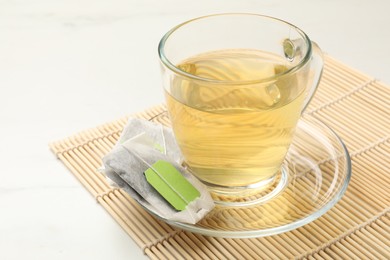 Photo of Tea bag and glass cup of hot beverage on white table, closeup. Space for text