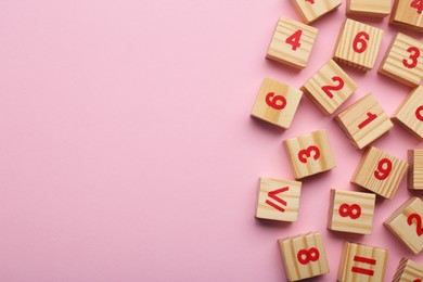 Wooden cubes with numbers and mathematical symbols on pink background, flat lay. Space for text