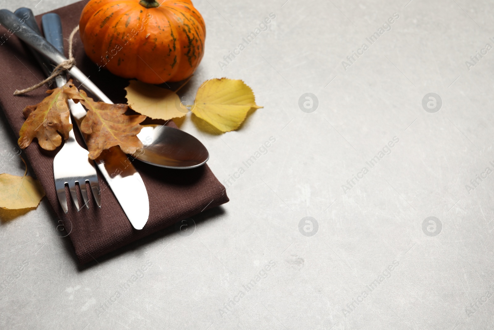 Photo of Cutlery, autumn leaves and pumpkin on light grey table, closeup. Space for text