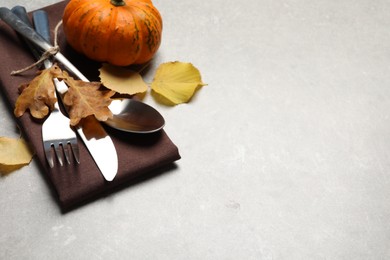 Photo of Cutlery, autumn leaves and pumpkin on light grey table, closeup. Space for text