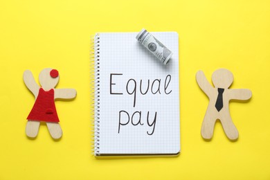 Photo of Equal pay. Open notebook, dollar banknote with wooden figures of man and woman on yellow background, flat lay