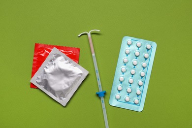 Photo of Contraception choice. Pills, condoms and intrauterine device on green background, flat lay