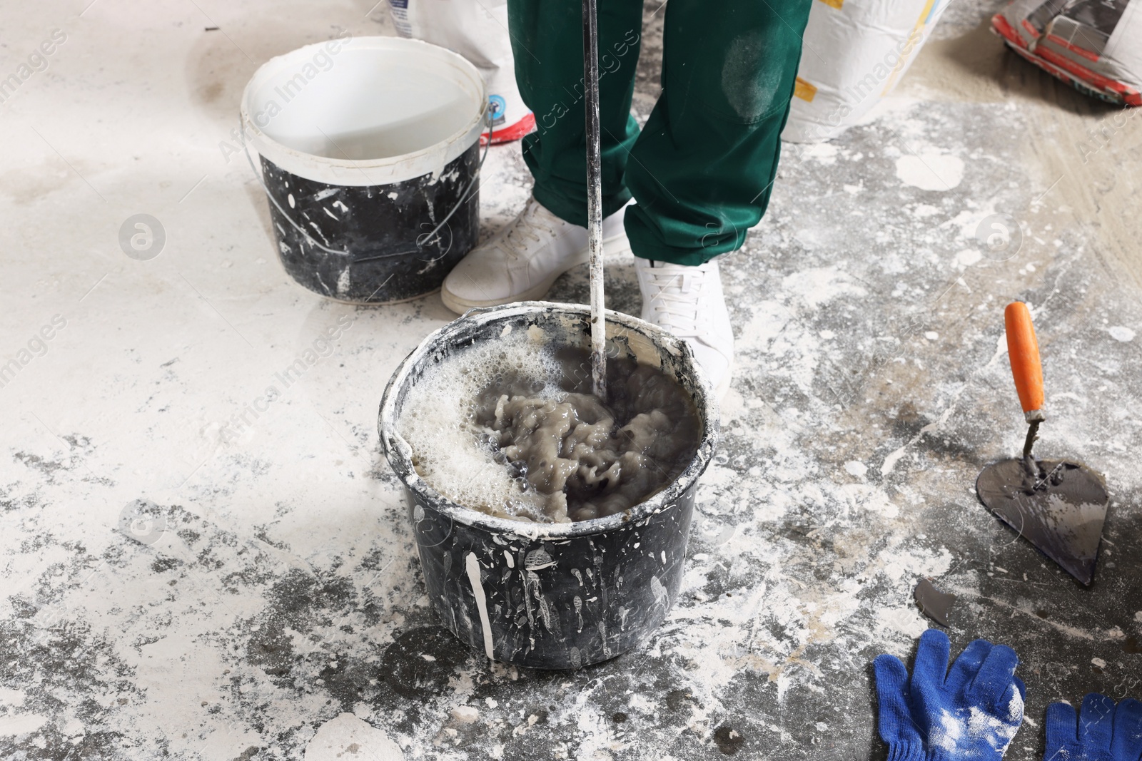 Photo of Worker mixing concrete in bucket indoors, closeup