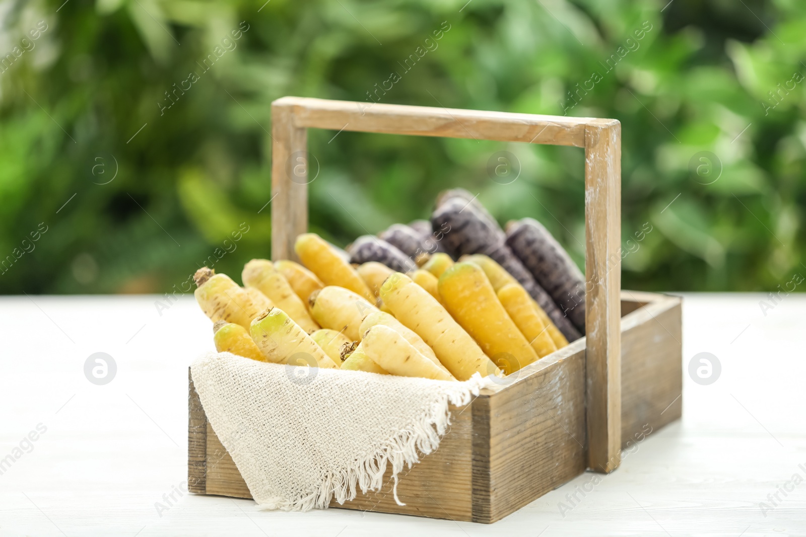 Photo of Different raw carrots in wooden basket on white table against blurred background